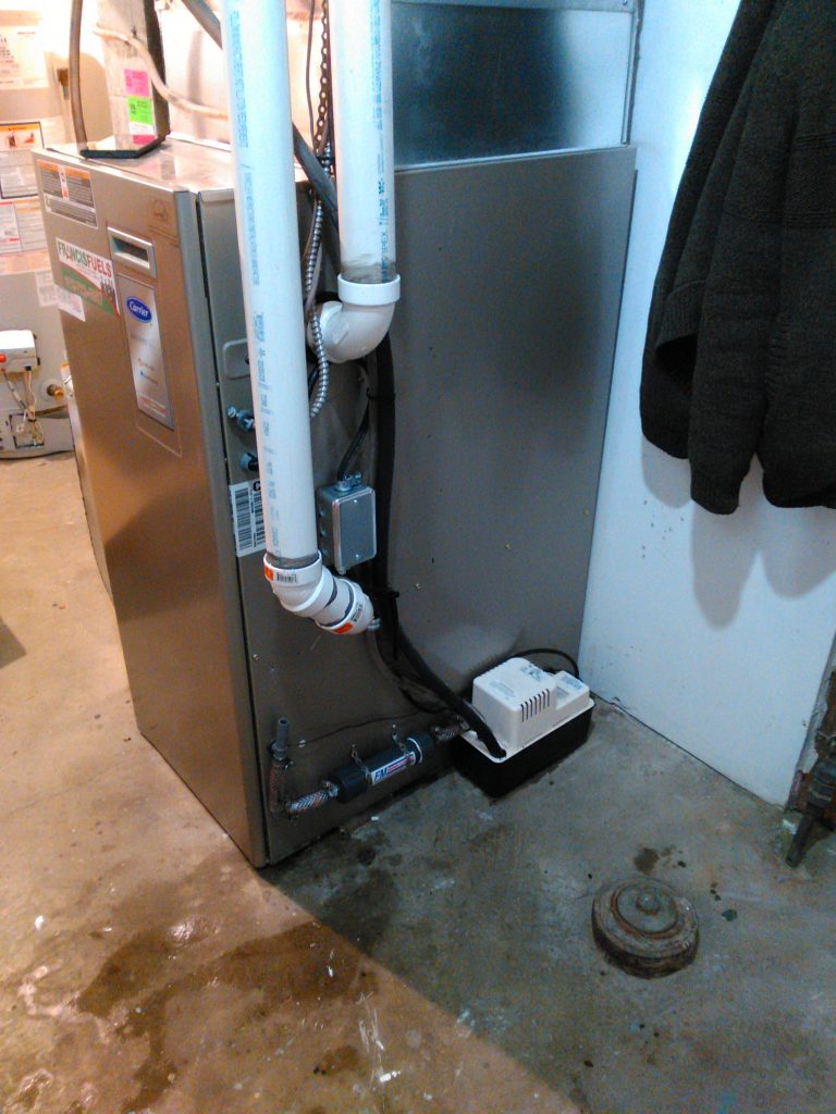 A gas furnace with white PVC venting and a condensate pump
